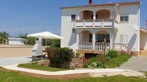 A two-story house with a balcony, a barbecue grill, and a garden area.