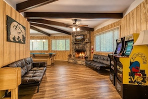 A cozy room with a pool table, leather sofas, a fireplace, and arcade games.