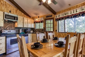 A rustic kitchen with wooden cabinets, a stone backsplash, and a dining table set for four. - Three Bears Den ·  Hot Tub,  Arcade games, $560 FREE tickets each paid day! (Gatlinburg)