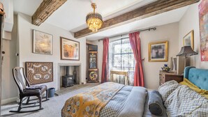 Un dormitorio con cama, un sillón mecedora, chimenea y obras de arte en las paredes.