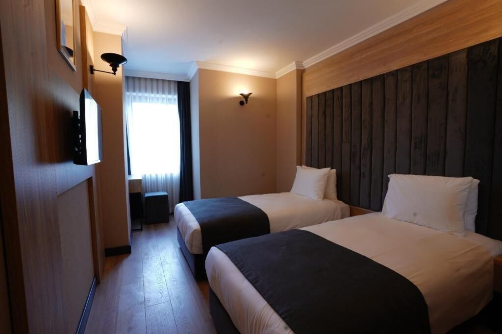 Une chambre d’hôtel avec deux lits, une tête de lit en bois, une petite table, un miroir et une fenêtre avec des rideaux.