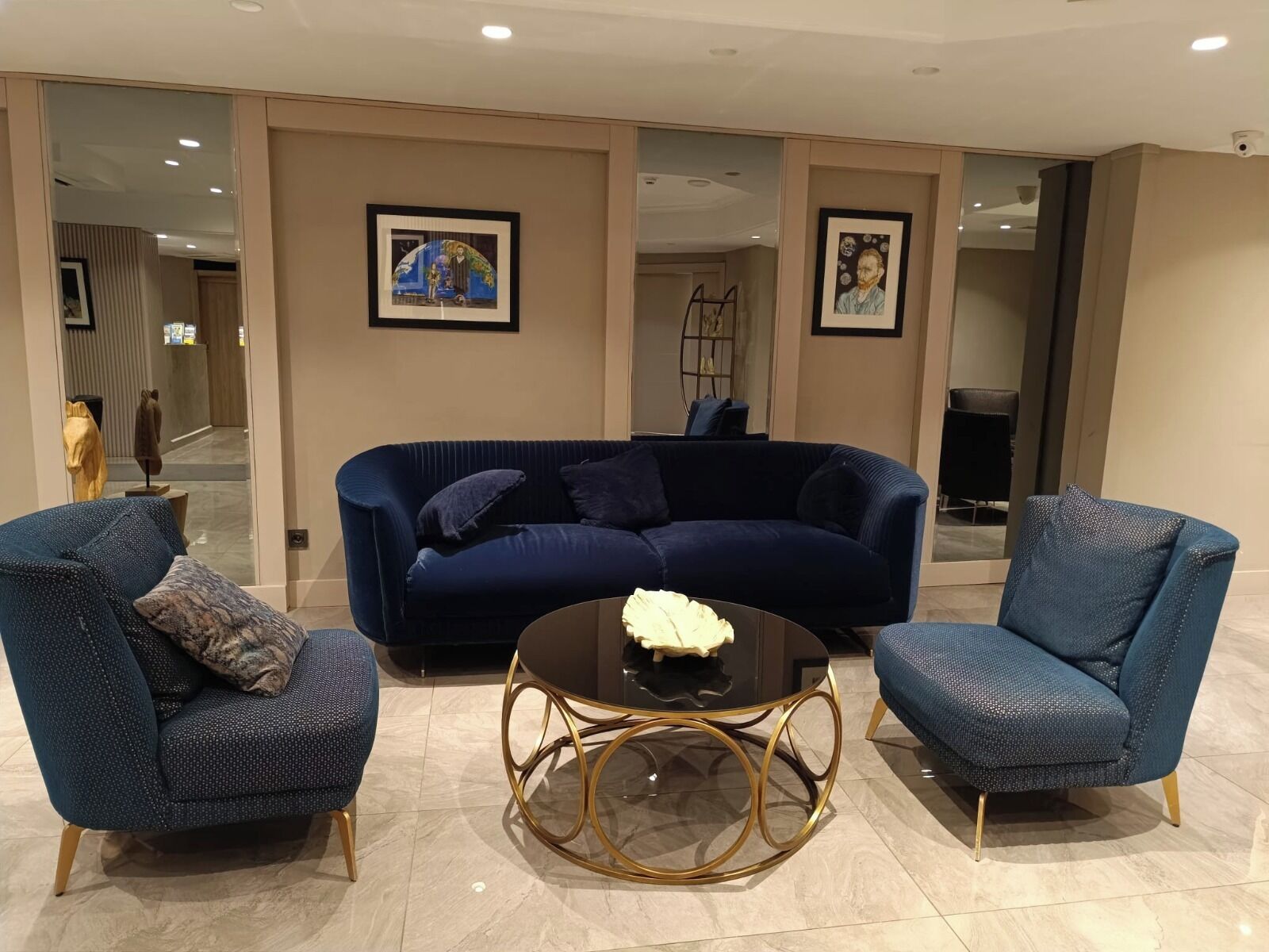 Un salon moderne avec un canapé bleu foncé, deux fauteuils assortis et une table basse ronde agrémentée de détails dorés.