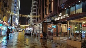 Um hotel com fachada moderna, restaurante à vista e rua molhada refletindo luzes.