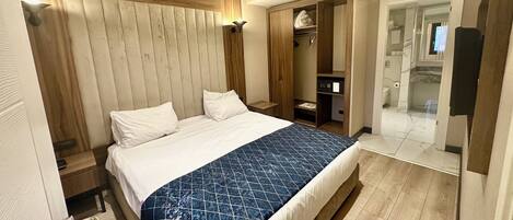A modern hotel room with a large bed, wooden headboard, built-in closet, and a walk-in shower.