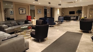 Uma sala de estar ampla com um sofá, poltronas, uma mesa de centro e uma televisão de tela plana na parede.