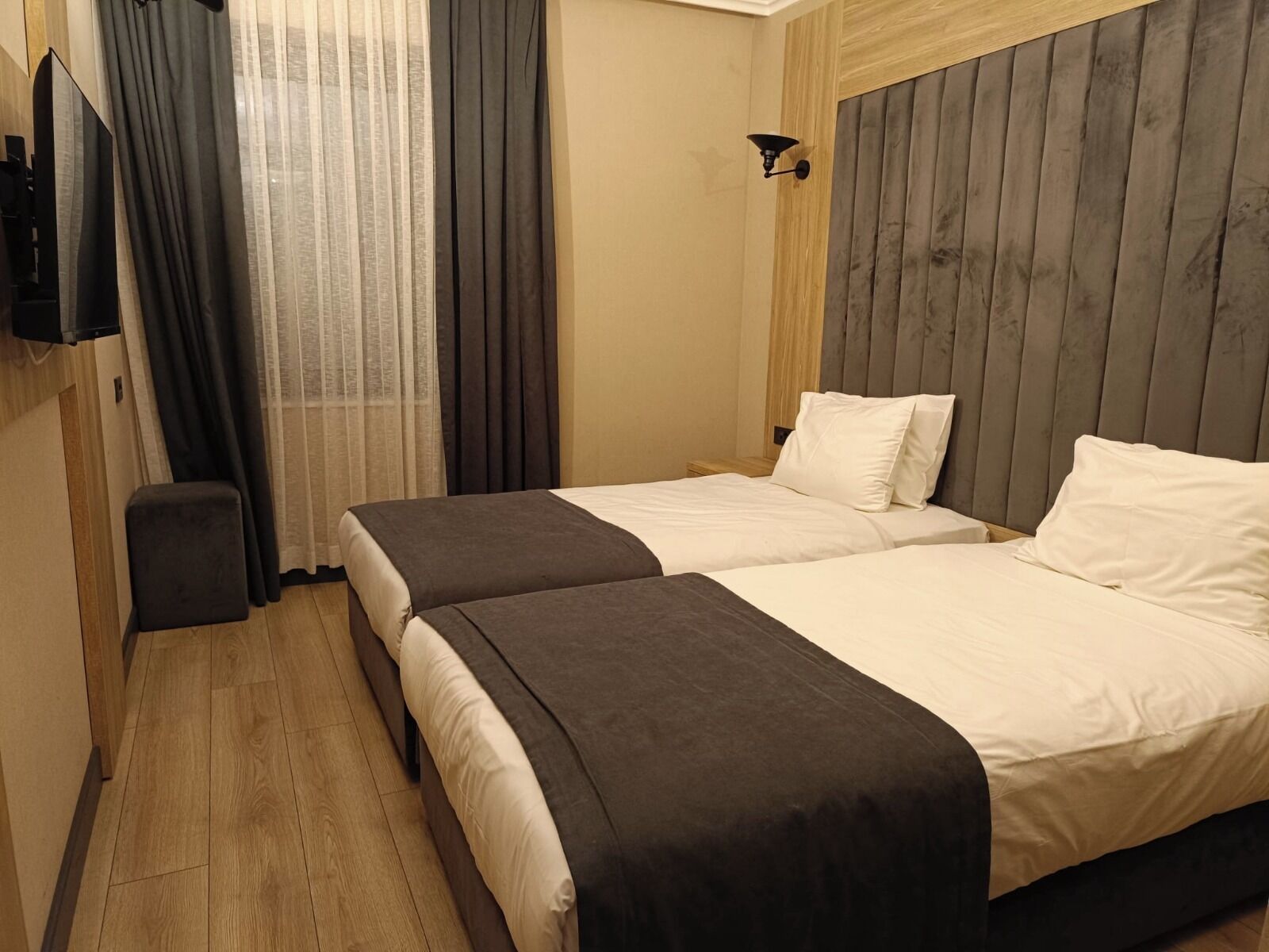 Une chambre d’hôtel avec deux lits, un petit coin salon, une télévision et une lampe fixée au mur.