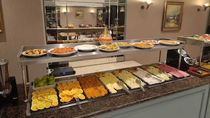 Um buffet com diversos tipos de comida e uma vitrine de vidro com frutas.