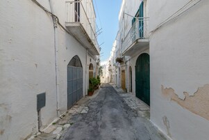 Una stretta via fiancheggiata da edifici bianchi con portali e finestre ad arco, che conduce a un punto centrale.