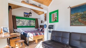 A cozy room with a bed, a couch, a table with stools, a window with curtains, and a painting on the wall. - Live Simply Cabin | Glamping at it's finest (Orderville)