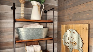 A wooden shelf unit with a metal bucket, a white pitcher, and a decorative tree cutout on a wooden wall. - Live Simply Cabin | Glamping at it's finest (Orderville)