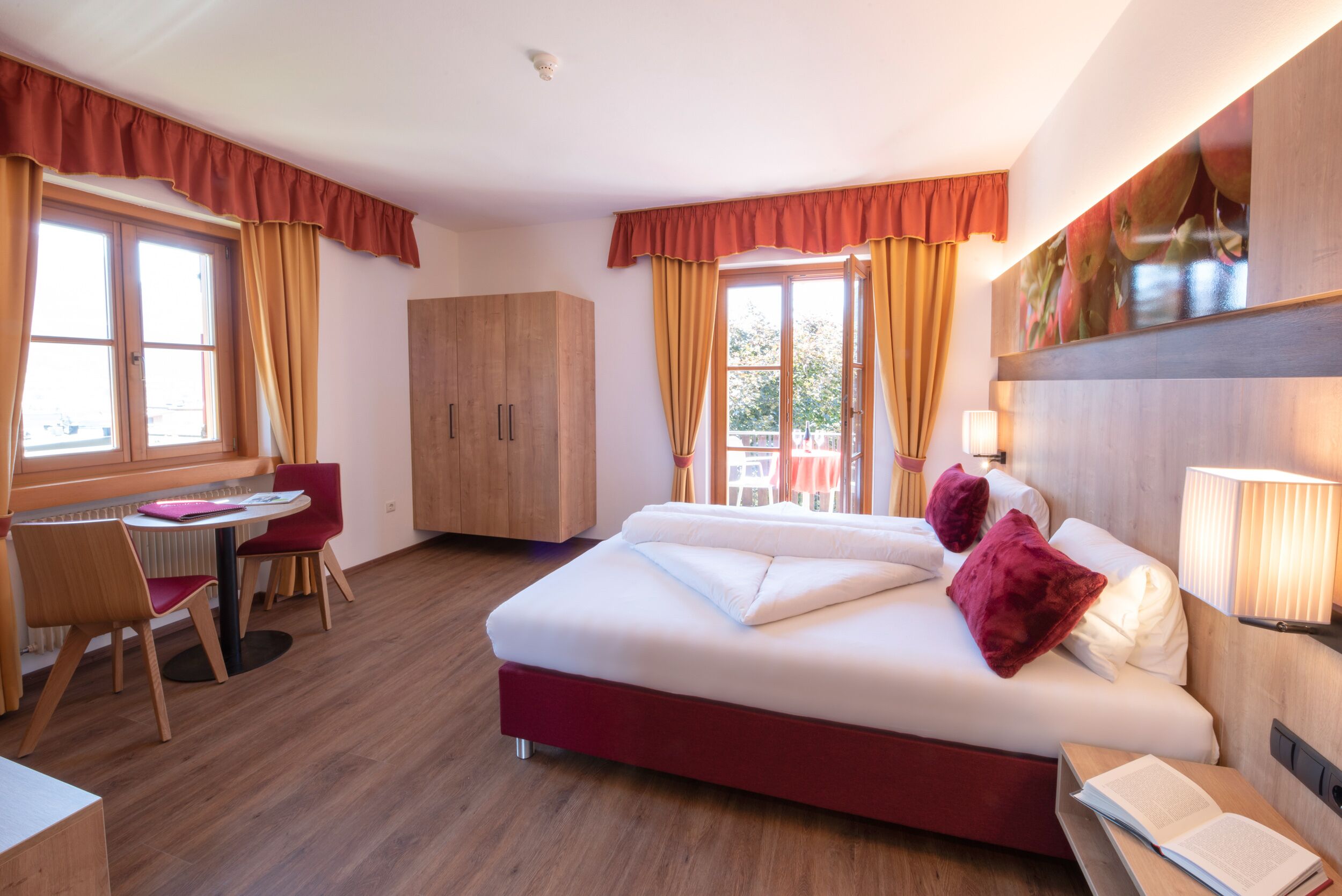 Habitación de hotel con cama, escritorio y silla. Tiene una ventana con cortinas, un armario de madera y una lámpara fijada a la pared.