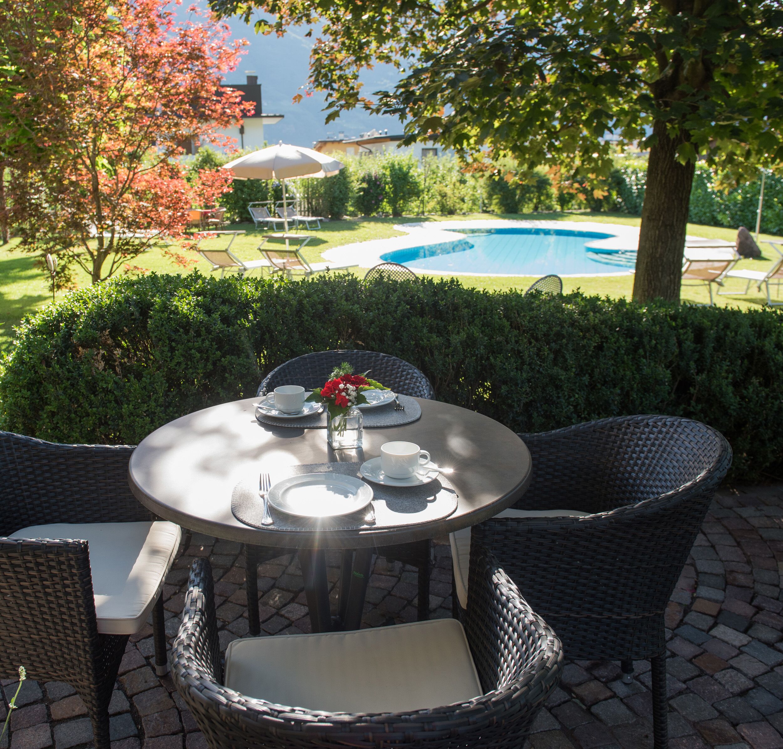 An outdoor dining area with wicker chairs and a round table set for four, overlooking a swimming pool.