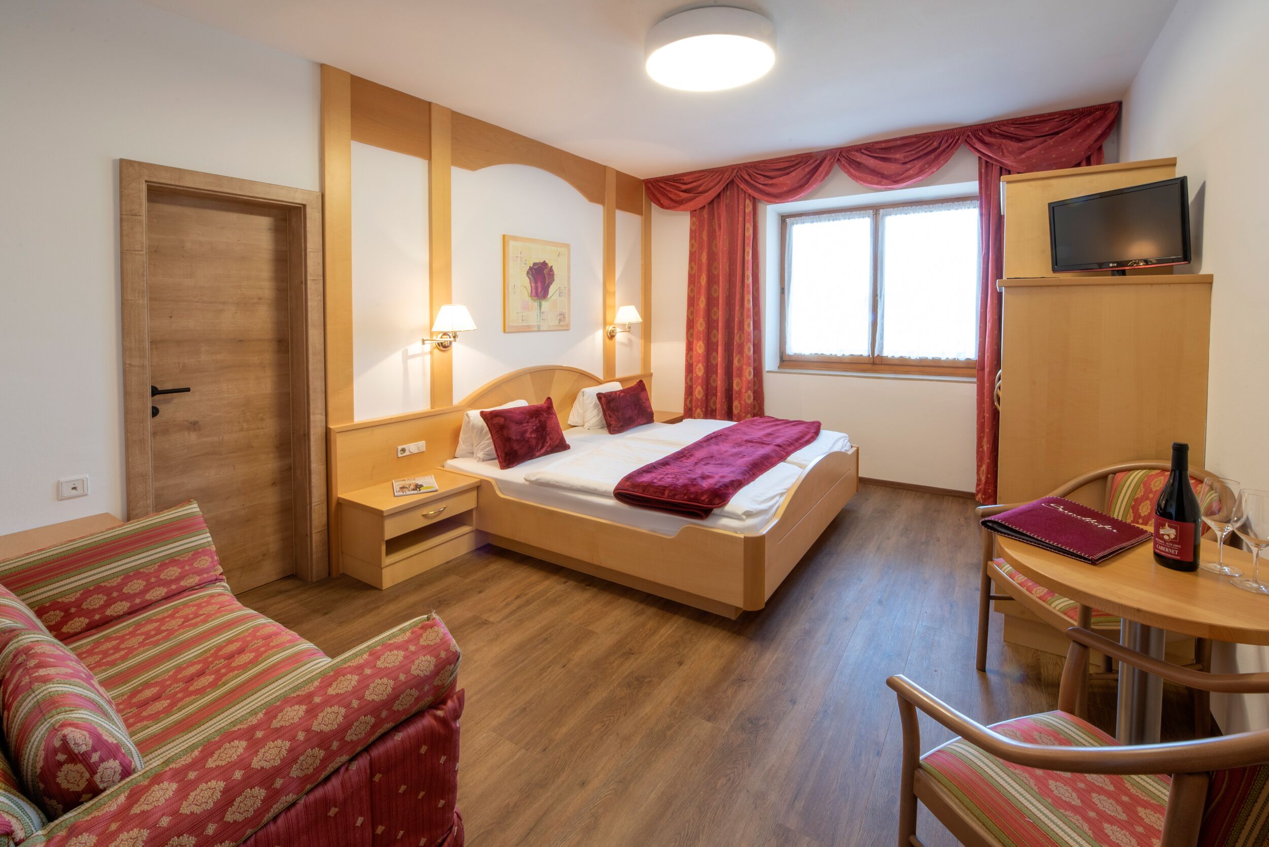 A hotel room with a bed, a desk, a chair, a TV, and a window with curtains.