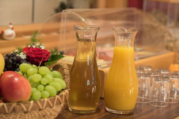 A breakfast setting with a fruit basket, two pitchers of beverages, and a row of glasses.