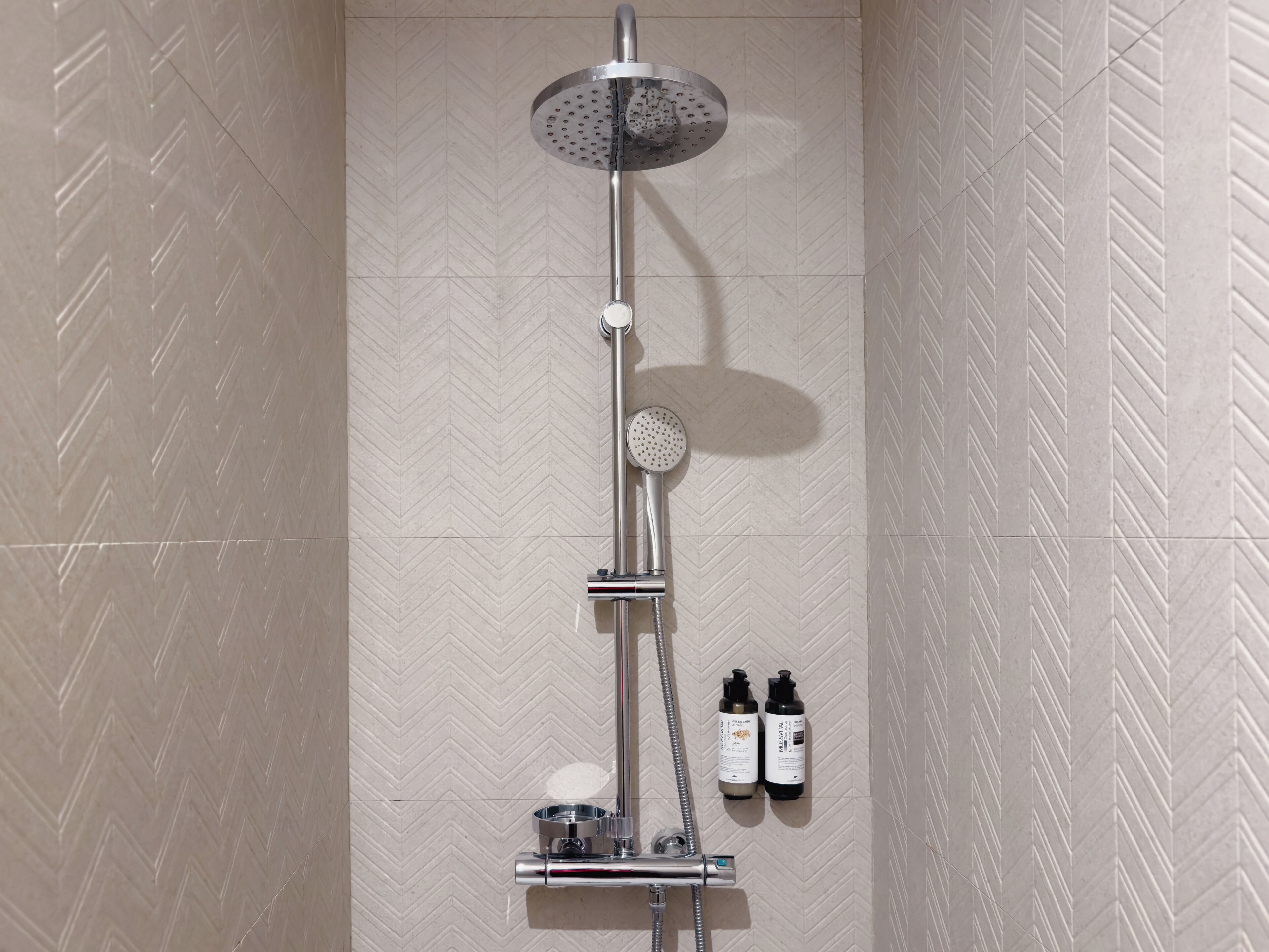 A shower with a rain showerhead, handheld showerhead, and two bottles of shampoo.