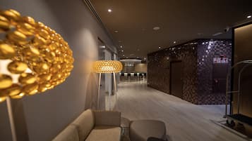 Eine moderne Hotelhalle mit einer Couch, einer besonderen goldenen Leuchte und einer Bar im Hintergrund.