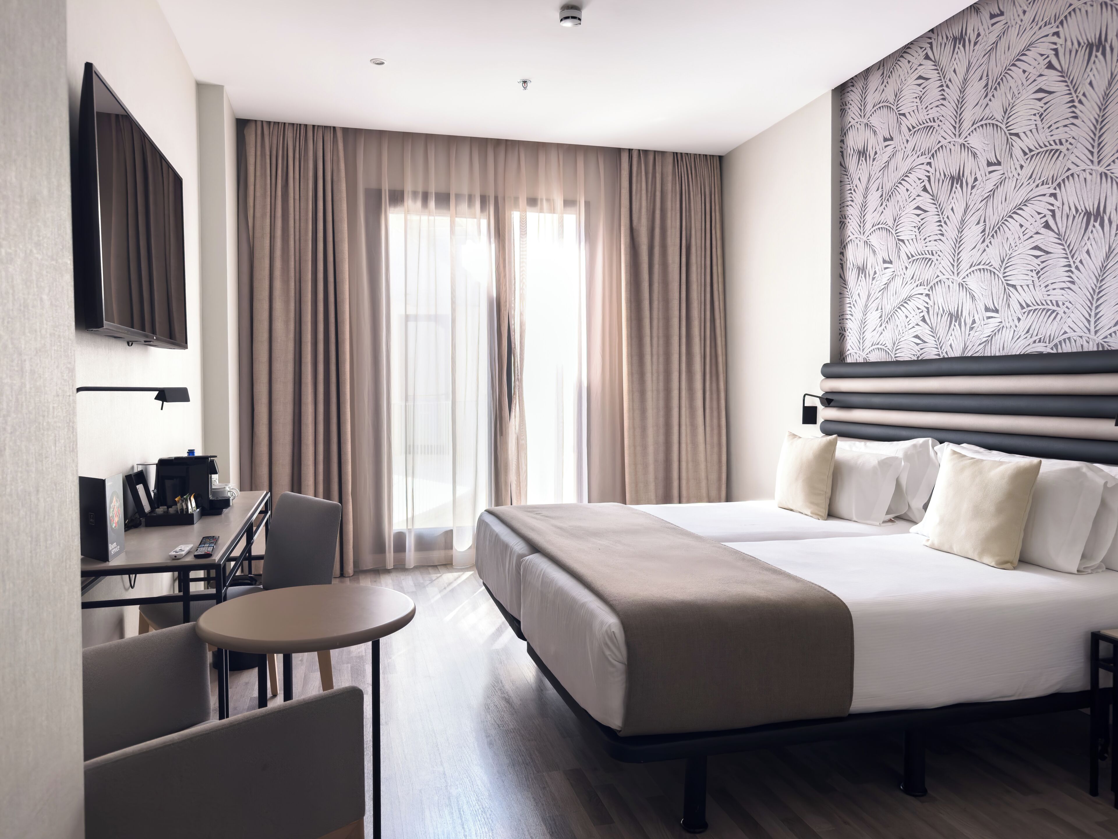 Une chambre d’hôtel équipée d’un lit, d’un bureau, d’une chaise, d’une petite table et d’un téléviseur fixé au mur.