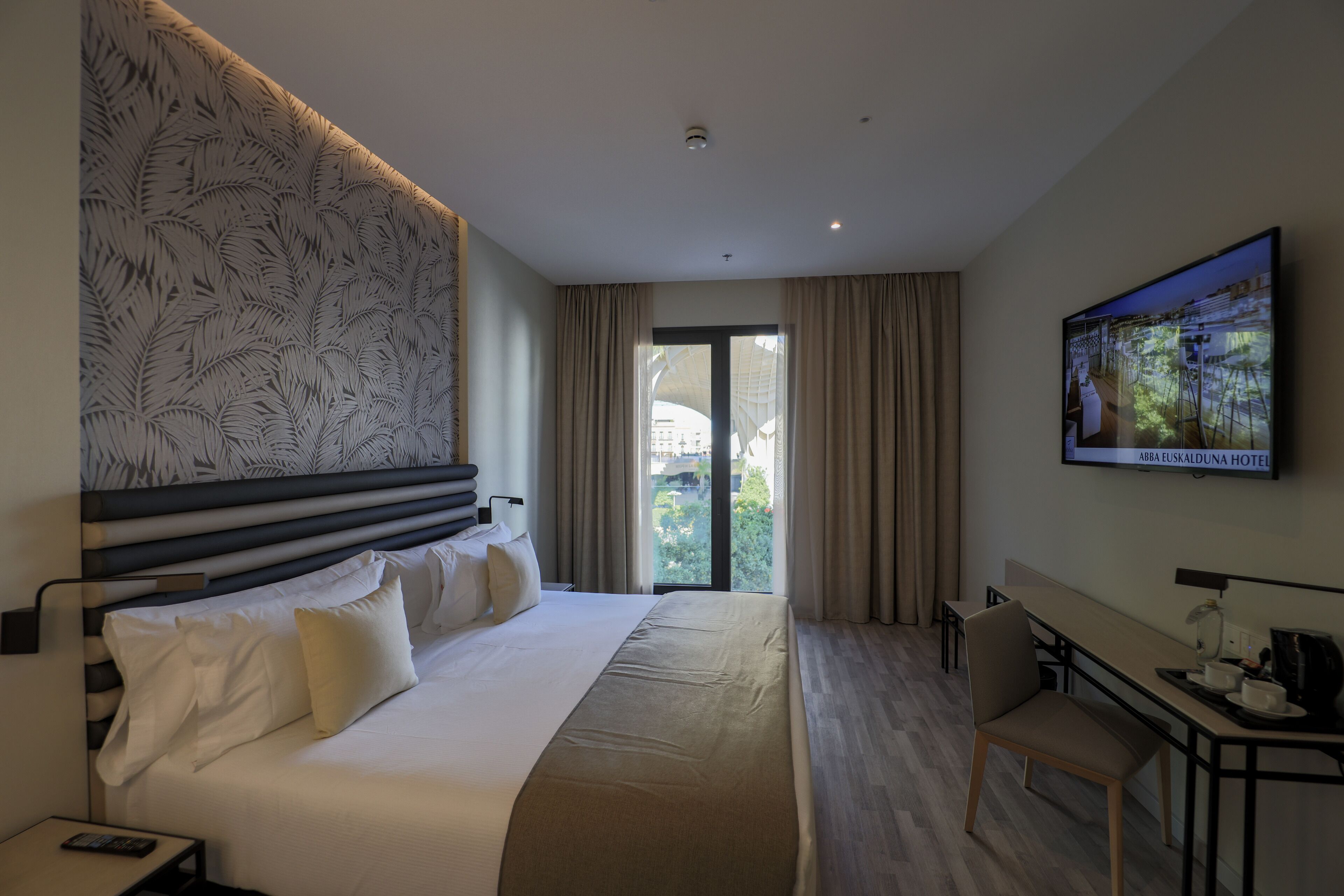 A hotel room with a large bed, a desk, a television, and a view of the outdoors.