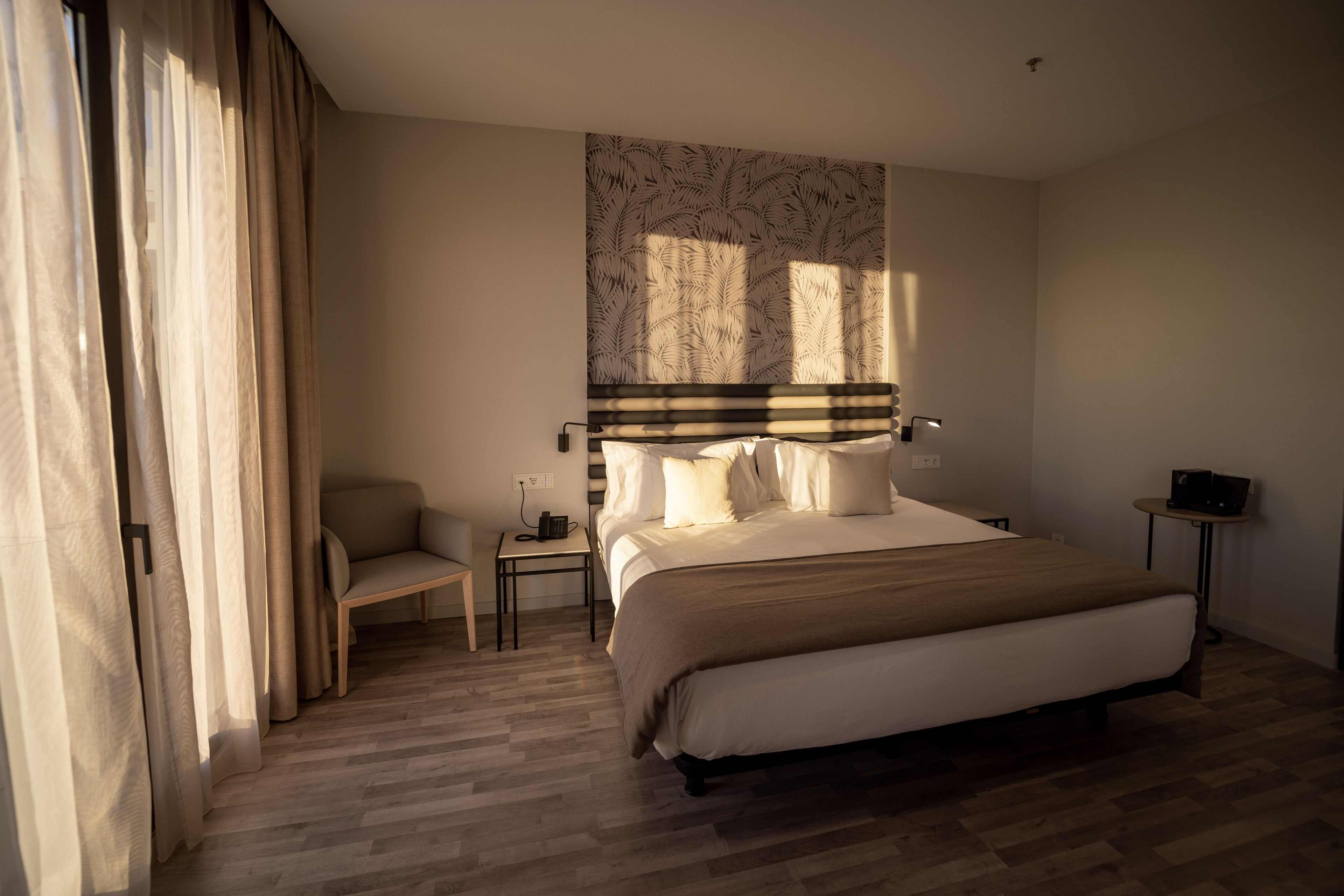 A bedroom with a large bed, a bedside table, a chair, and a wall-mounted lamp.