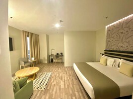 Habitación de hotel moderna con una cama grande, un escritorio con una silla, una mesita y un cabecero estampado.
