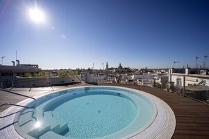 Una piscina en la azotea con vistas a la ciudad, rodeada por una terraza de madera y barandillas de metal.