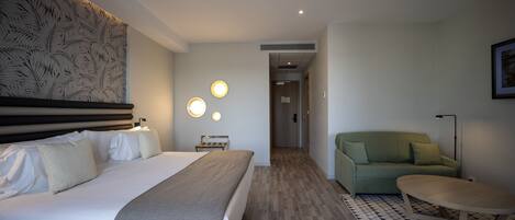 Una habitación de hotel con una cama grande, un sofá verde, una mesita pequeña y una alfombra estampada.