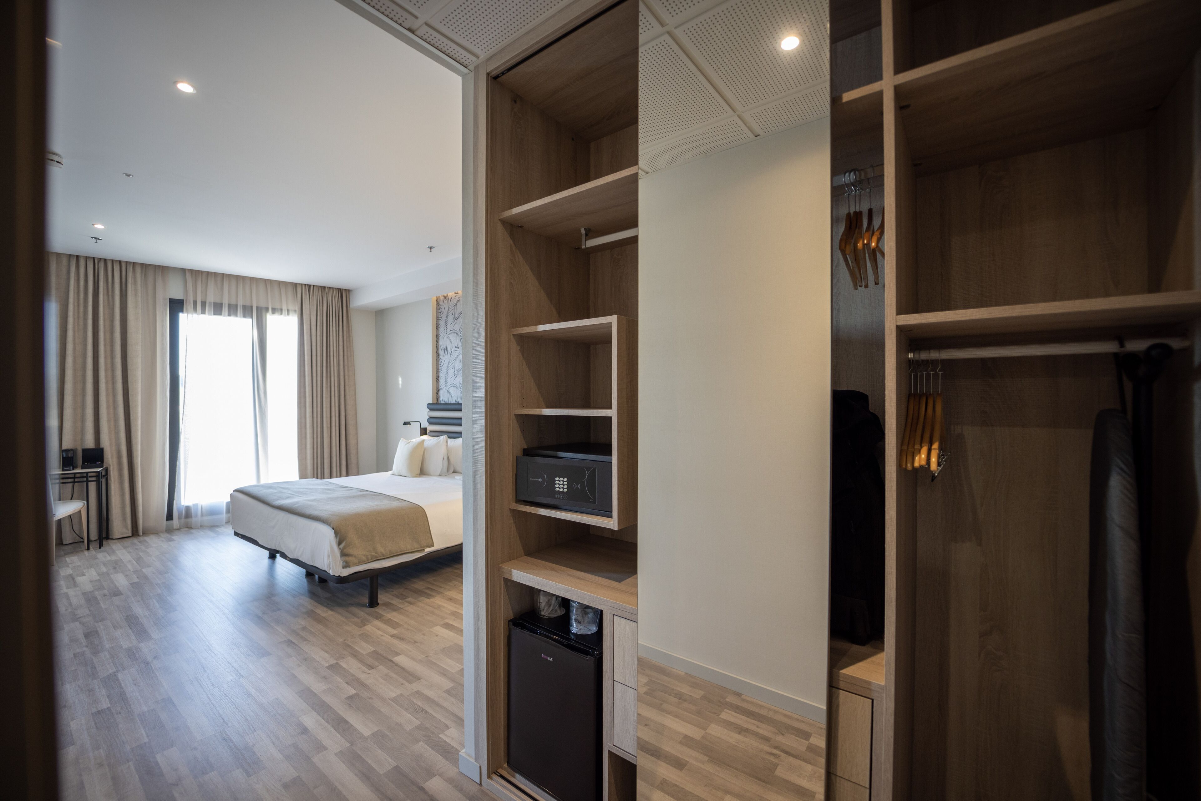 A hotel room with a bed, a desk, a wardrobe, and a mini-fridge.