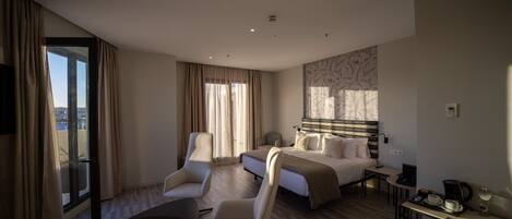 Ein modernes Hotelzimmer mit einem Bett, zwei Sesseln, einem kleinen Tisch und einer Kaffeestation.