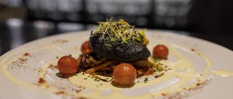 A plate of food with a dark, round item in the center, surrounded by smaller round items and garnished with green sprouts.