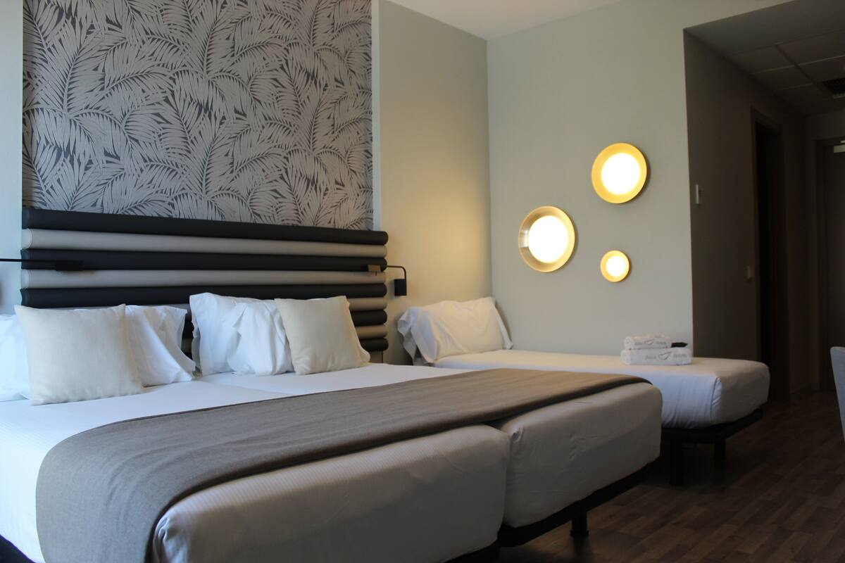 A hotel room with two beds, a patterned wallpaper, and a wall-mounted light fixture.