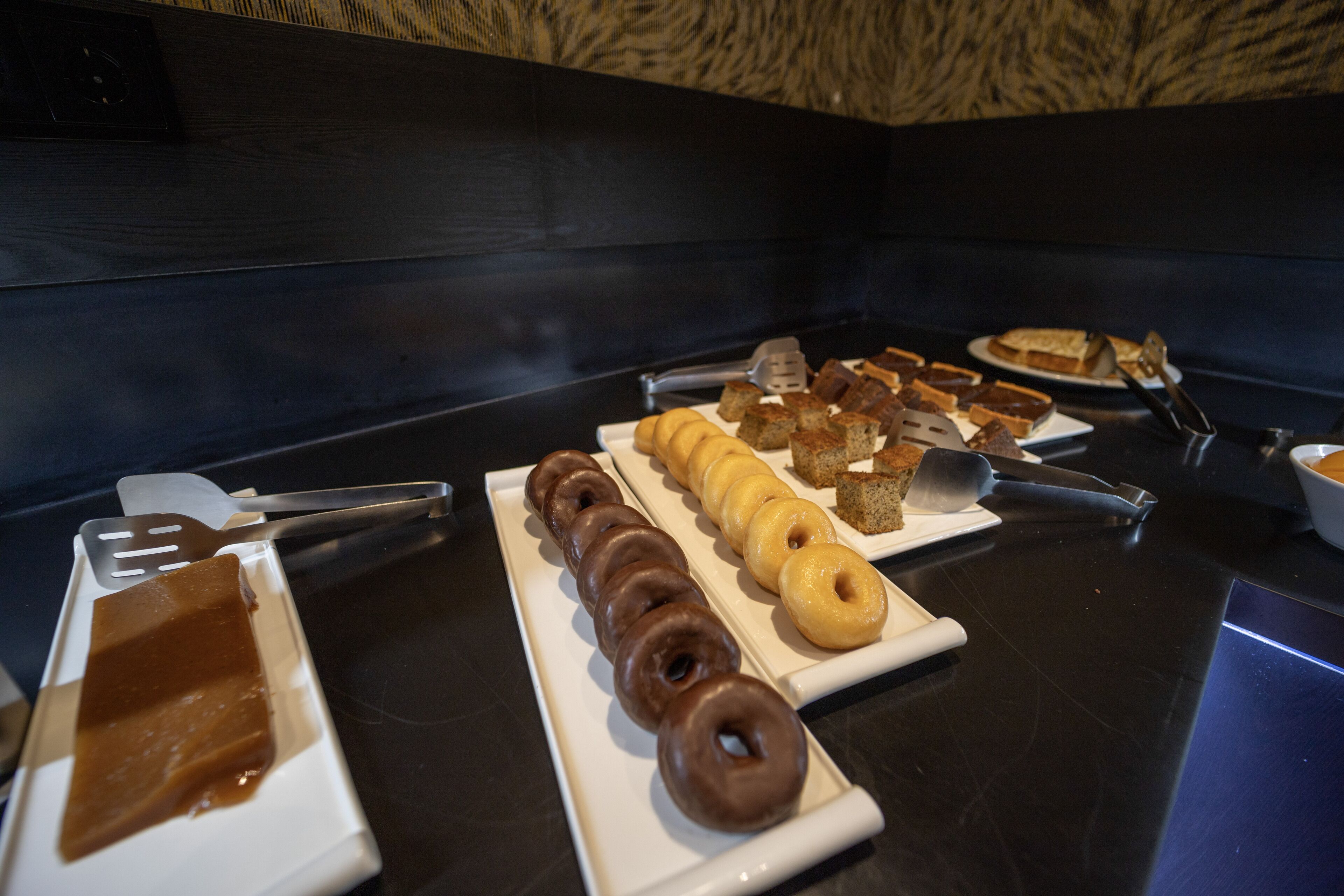 Un bufé con diversos pasteles y postres, incluyendo rosquillas y tartas, dispuestos en platos blancos.