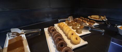 Un bufé con diversos pasteles y postres, incluyendo rosquillas y tartas, dispuestos en platos blancos.