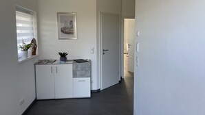 A modern hallway with a white door, a small window with blinds, and a potted plant on a shelf. - Ferienwohnung im Pfalz (Lustadt)