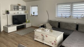 A modern living room with a flat-screen TV, a white entertainment unit, a grey sofa, and a patterned rug. - Ferienwohnung im Pfalz (Lustadt)
