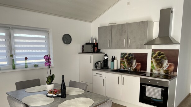 A modern kitchen with a dining area, featuring a large island, white cabinets, and a stainless steel range hood. - Ferienwohnung im Pfalz (Lustadt)
