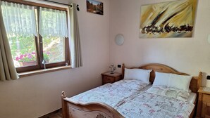 Un dormitorio con una cama de madera, una ventana con cortinas, una mesita de noche y un cuadro en la pared.