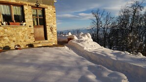 Un edificio de piedra con techo nevado y vista a árboles cubiertos de nieve al fondo.