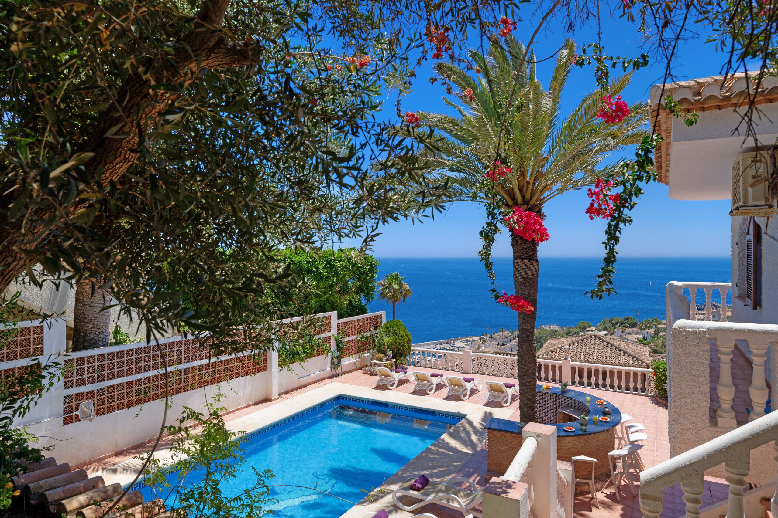 A pool area with a view of the sea, surrounded by palm trees and lounge chairs.