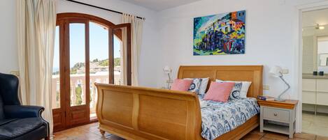 A bedroom with a wooden bed, a nightstand, a chair, a ceiling fan, and a painting on the wall.