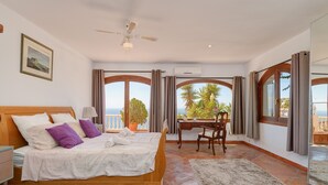 A bedroom with a bed, a desk, and a view of the sea.