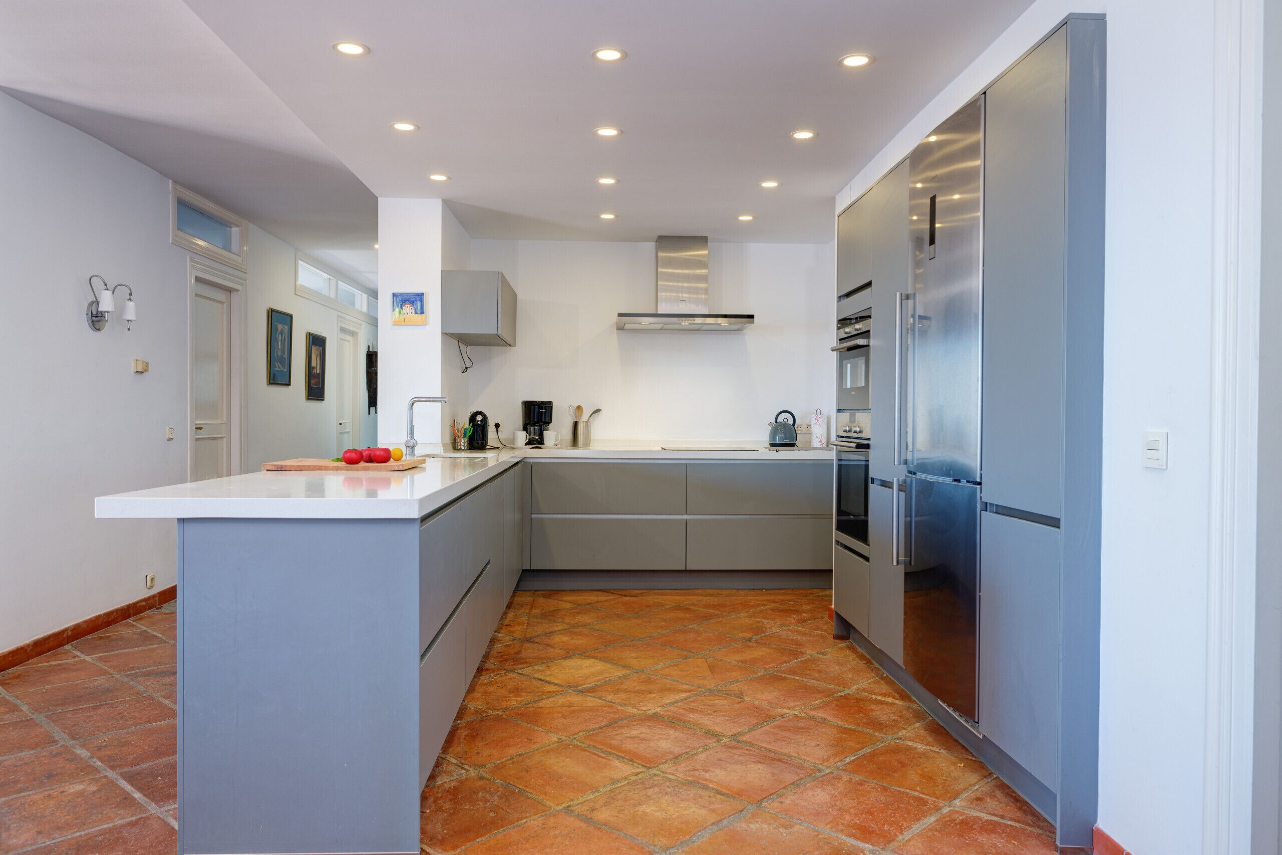 A modern kitchen with a central island, grey cabinets, stainless steel appliances, and a tiled floor.