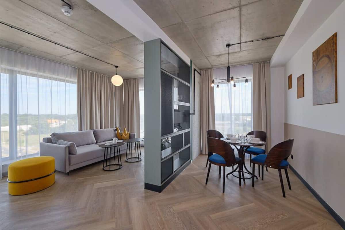 A modern living room with a sofa, ottoman, dining table, chairs, and a bookshelf.