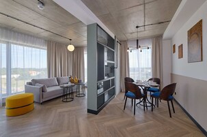 A modern living room with a sofa, ottoman, dining table, chairs, and a bookshelf.