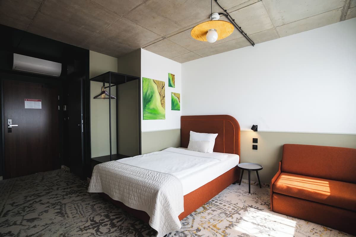 A hotel room with a bed, a chair, a small table, and a wardrobe.