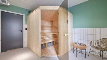Una sauna de madera con puerta, pared de azulejos y una mesa de mimbre con vasos.