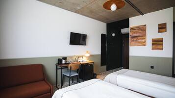 Habitación de hotel con una cama, un escritorio con silla, un televisor y obras de arte en la pared.