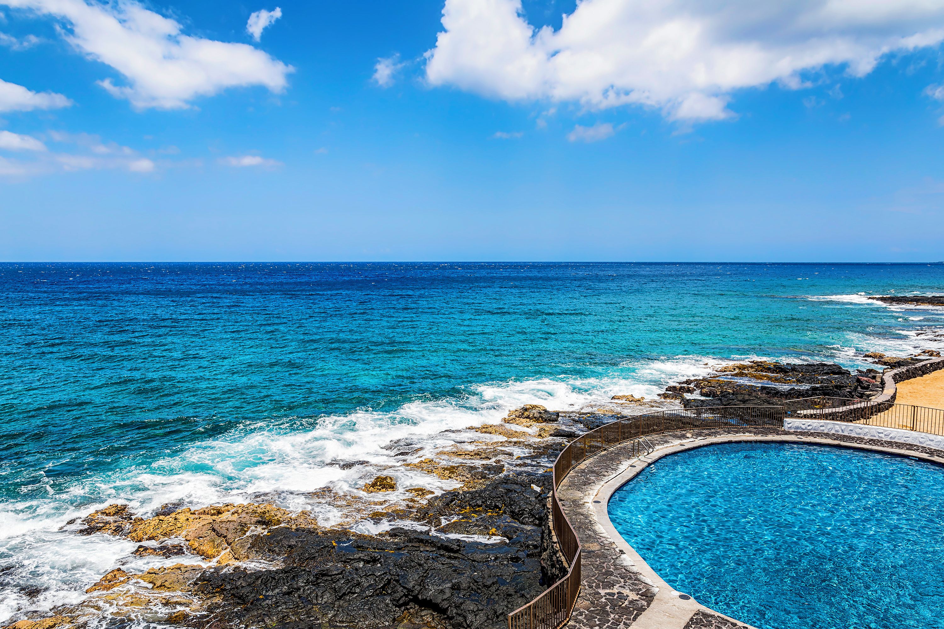 A pool adjacent to a rocky coastline with the ocean in the background.