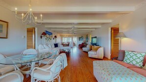 A spacious living room with a glass dining table, white sofas, and a TV. - Bring your Family, Oceanfront, 8 bedroom, 4 bathroom, private boardwalk! (Isle of Palms)