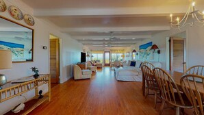 A spacious living room with a wooden floor, a dining area with wooden chairs, a sofa set, and a television. - Bring your Family, Oceanfront, 8 bedroom, 4 bathroom, private boardwalk! (Isle of Palms)
