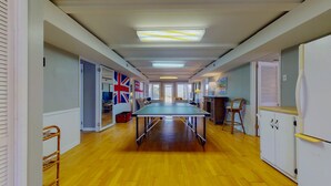 A spacious room with a ping pong table, wooden flooring, and a view of the outdoors. - Bring your Family, Oceanfront, 8 bedroom, 4 bathroom, private boardwalk! (Isle of Palms)